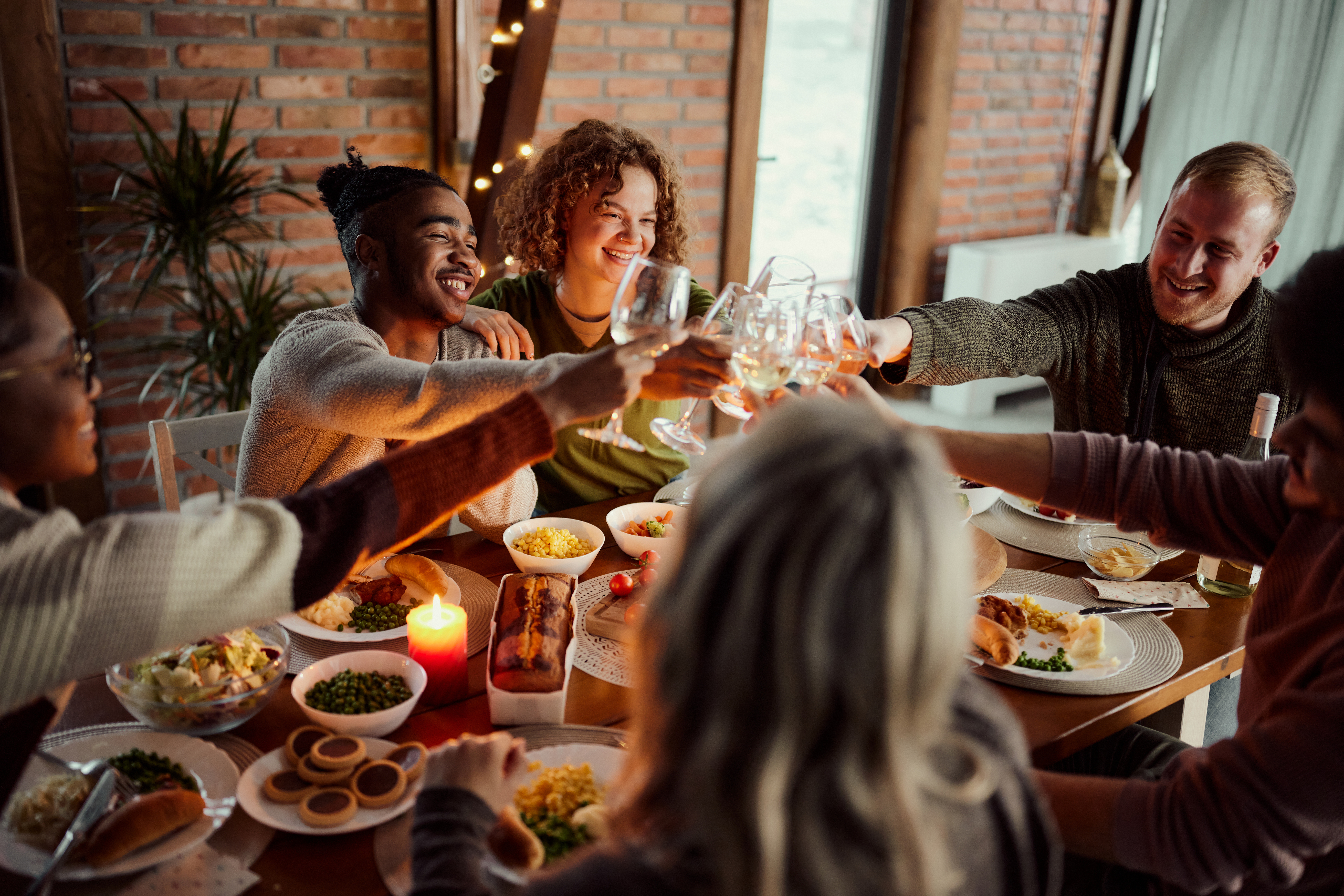 Group of happy friends having fun while toasting with white wine during a meal at dining table.