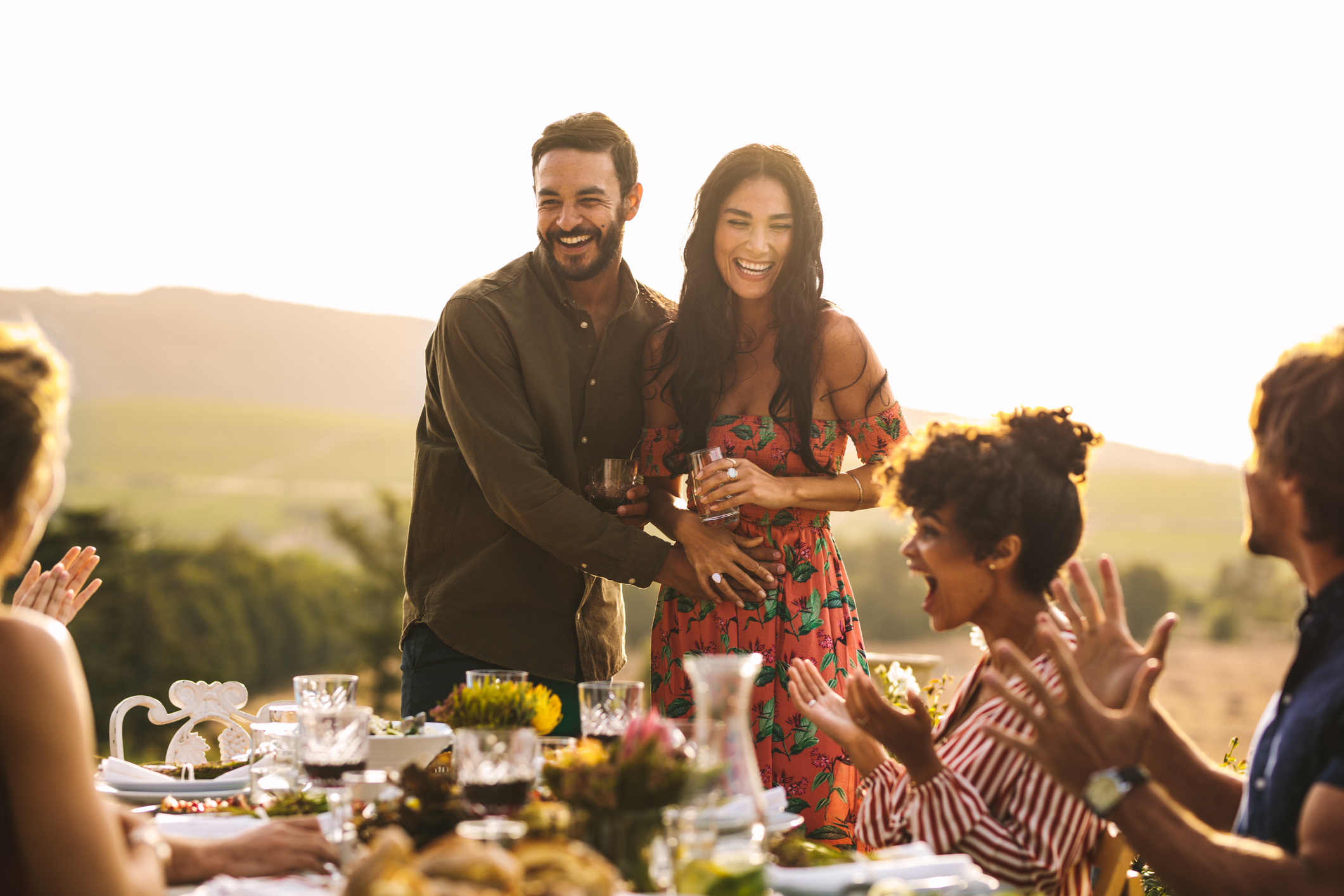 Happy young couple announcing their pregnancy at a party. Man with his girlfriend sharing surprise pregnancy announcement with friends at dinner party.